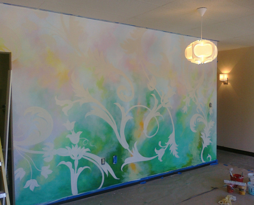Reception mural in soft greens and warm yellows behind the front desk at The Still Point Yoga